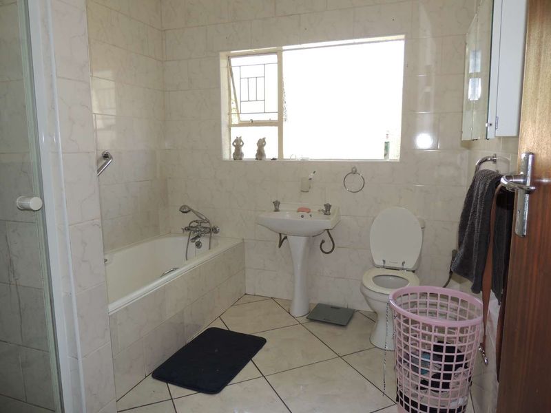 A functional bathroom featuring a bathtub, pedestal sink, toilet, and tiled finishes, offering a practical layout with natural light from the window.