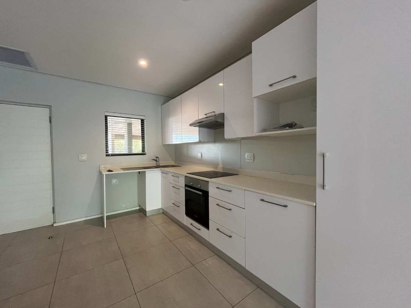 Modern kitchen featuring white high-gloss cabinetry, stone countertops, integrated oven and hob, and neutral tiled flooring in a clean, minimalist space.