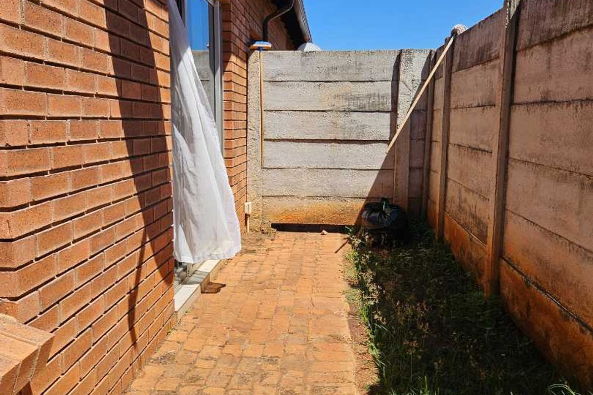A narrow side exterior area featuring red brick paving, enclosed by precast concrete boundary walls and accessible via a sliding glass door.