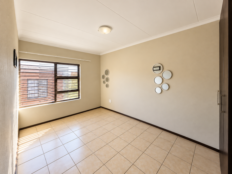 A bright, empty bedroom featuring neutral tiled flooring, a built-in cupboard, and venetian blinds, offering a clean and versatile space.
