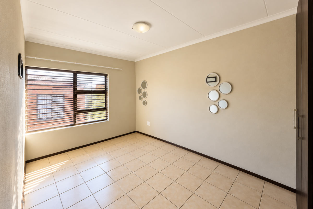 A bright, empty bedroom featuring neutral tiled flooring, a built-in cupboard, and venetian blinds, offering a clean and versatile space.