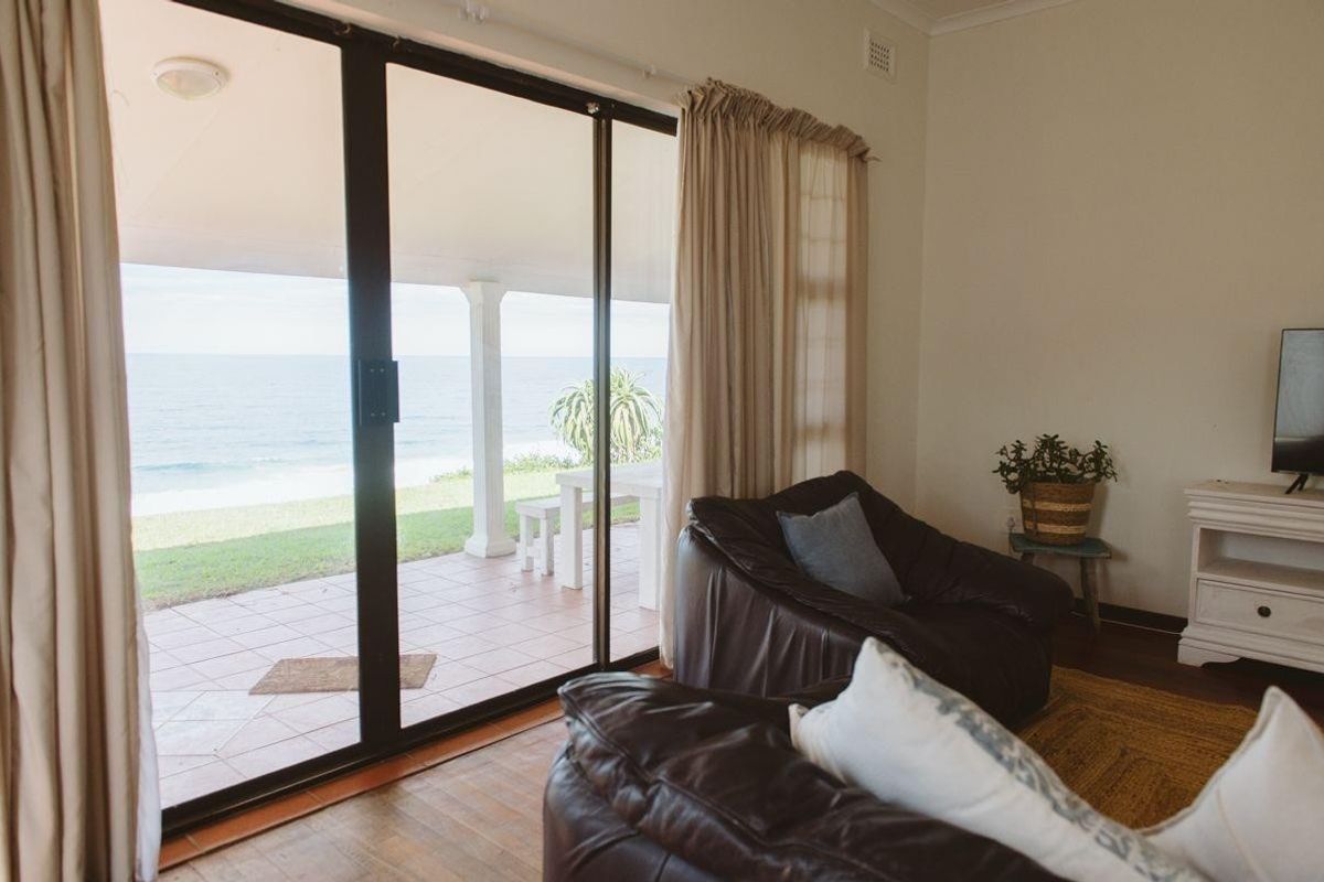 A comfortable living room featuring large sliding glass doors that open onto a tiled patio with direct ocean views.