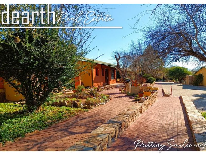 A well-maintained retirement village exterior featuring a paved walkway, stone retaining walls, and established garden landscaping leading to the residential units.