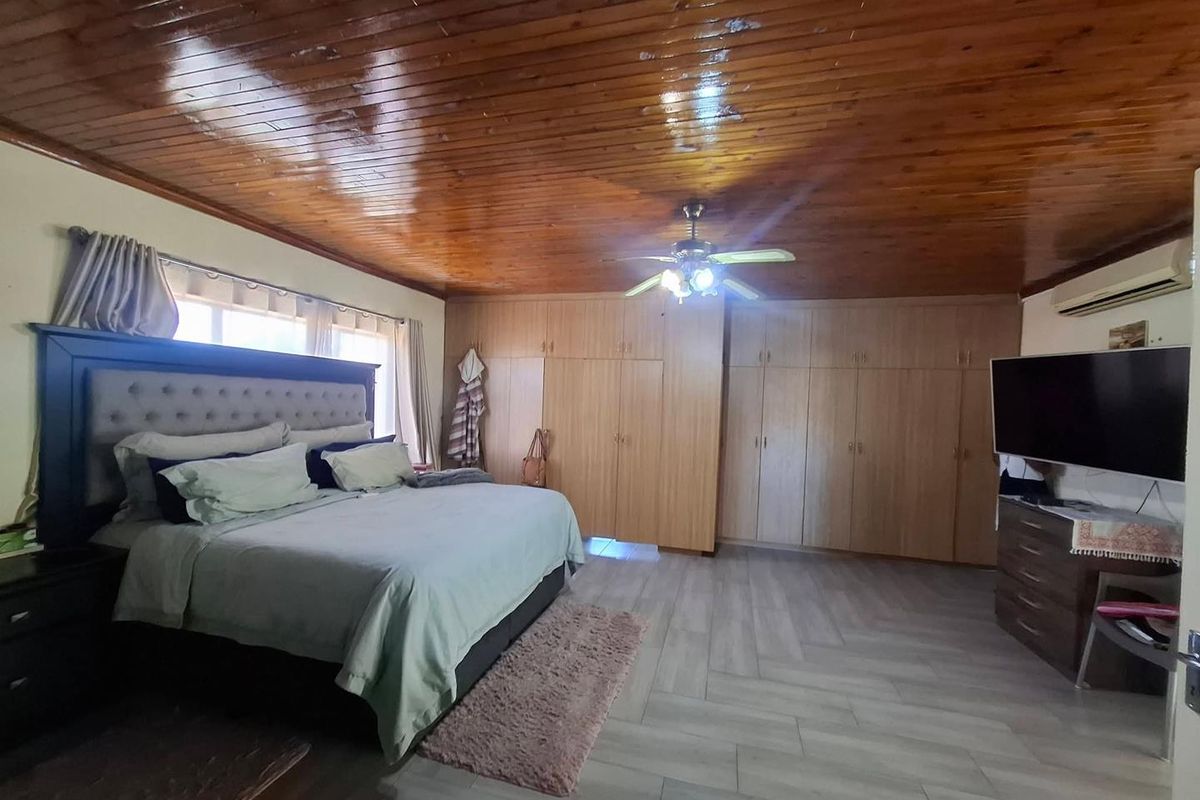 Spacious bedroom featuring a high-gloss timber-clad ceiling, extensive built-in cabinetry, and modern light-toned floor tiling.