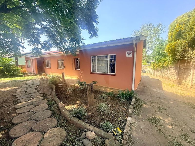 Front exterior view of a single-story house featuring a concrete driveway, stone pathway, and established garden area with a brick boundary wall.