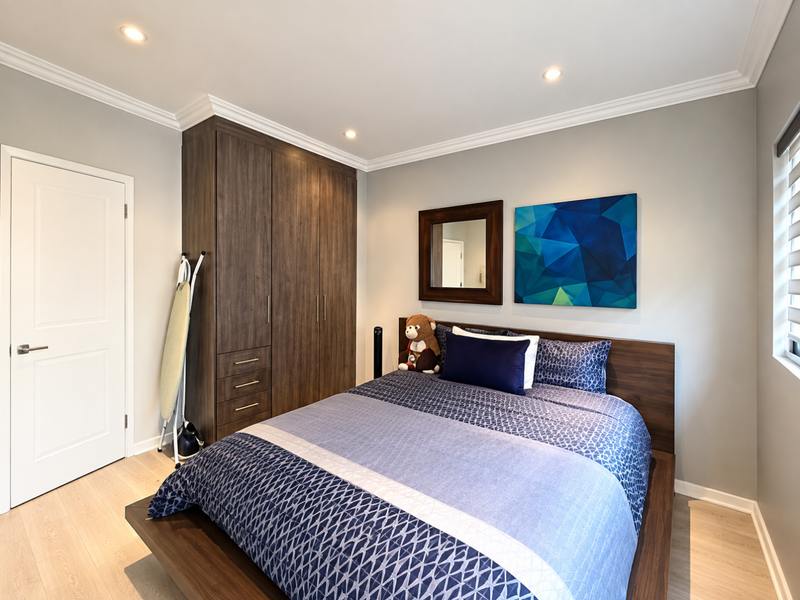 A well-maintained bedroom featuring built-in dark wood cupboards, recessed downlighting, crown molding, and light-toned laminate flooring.