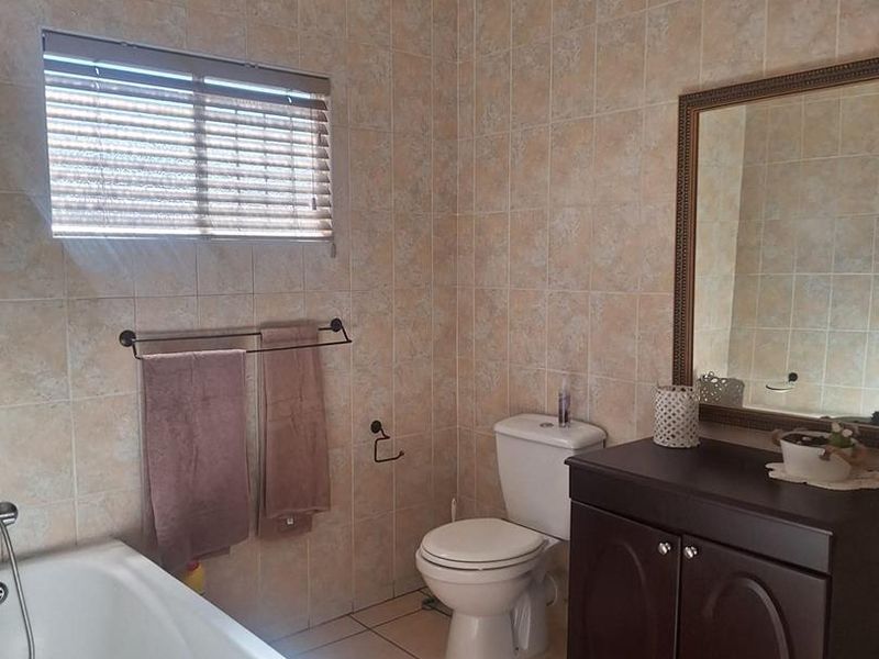 A functional bathroom featuring a bathtub, toilet, and vanity cabinet with wall-to-wall tiling.