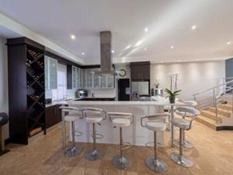 Modern open-plan kitchen featuring a large island with breakfast bar seating, integrated wine storage, and sleek cabinetry, adjacent to a staircase.
