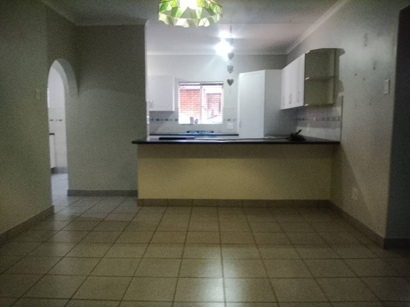 An open-plan living and kitchen area featuring tiled flooring, a breakfast bar, and an arched entryway, presenting a blank canvas for renovation.