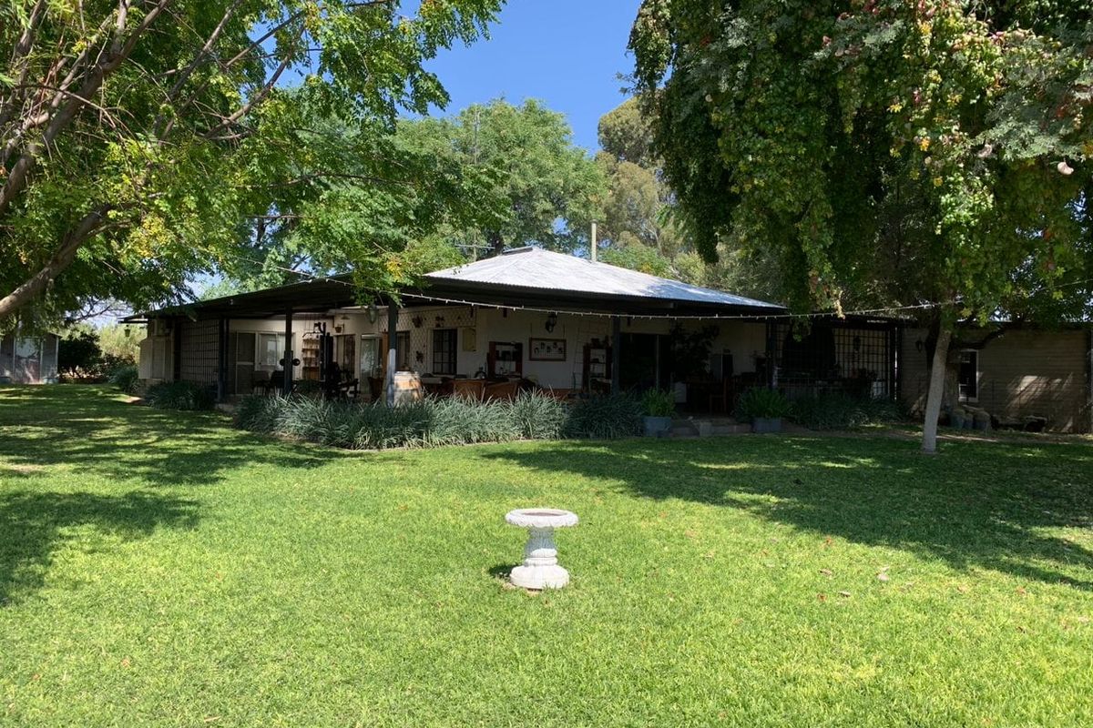 A view of the rear elevation of the farmhouse, featuring a wide covered patio area overlooking a spacious, well-maintained garden with mature trees.