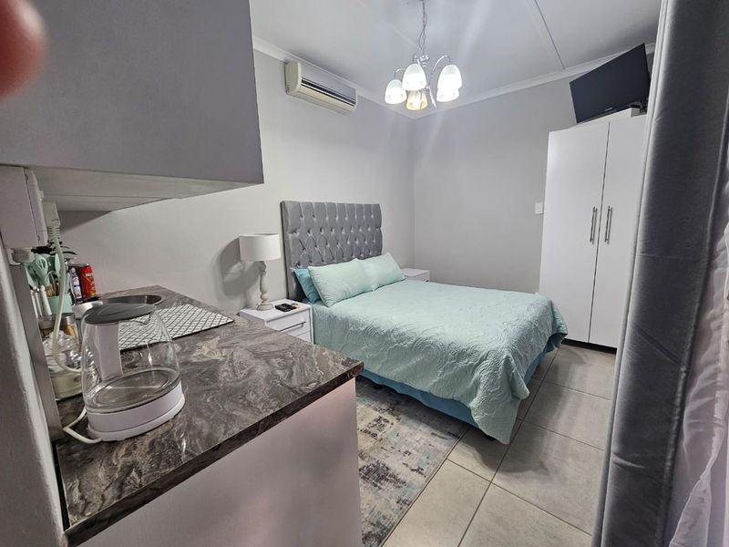 Compact open-plan studio apartment featuring a kitchenette, tiled flooring, built-in wardrobe, and a wall-mounted air conditioning unit.