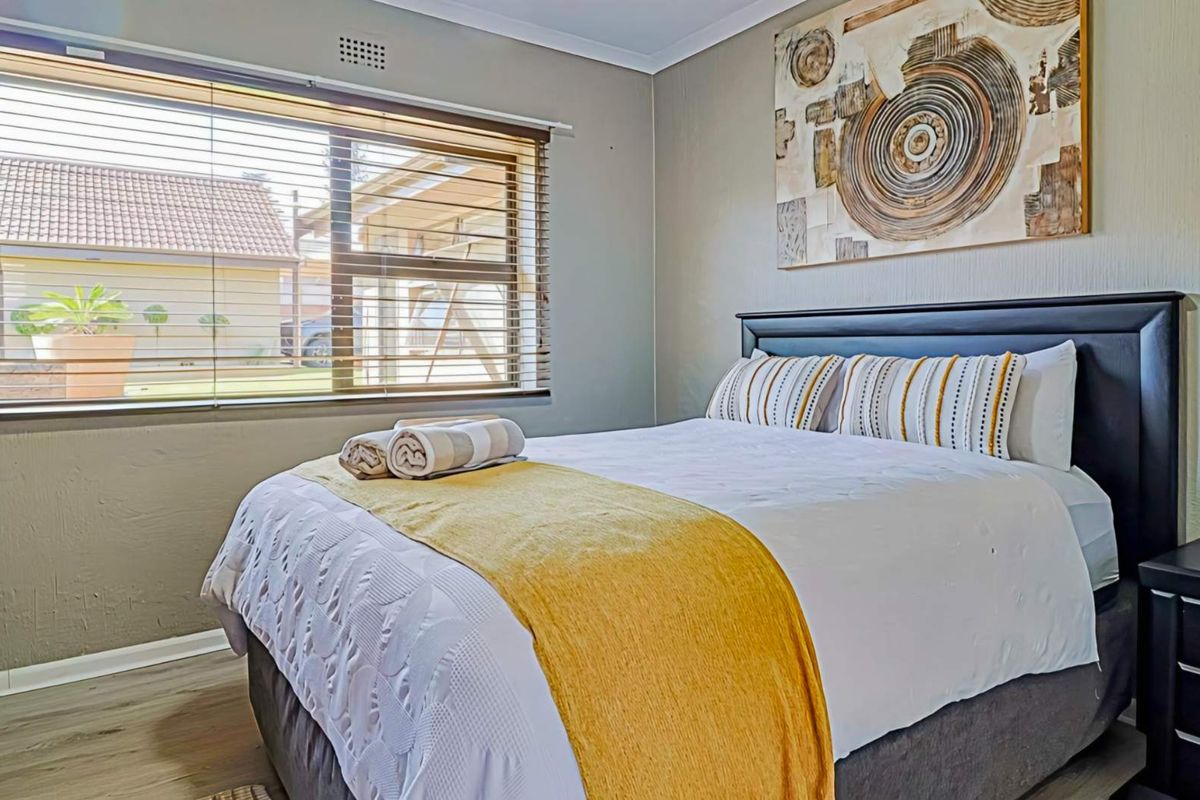 A well-maintained bedroom featuring laminate flooring, neutral wall tones, and a large window fitted with venetian blinds.
