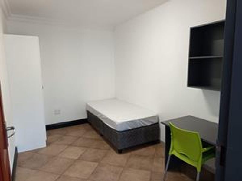A functional bedroom featuring tiled flooring, a built-in wardrobe, and wall-mounted shelving, providing a practical living space.