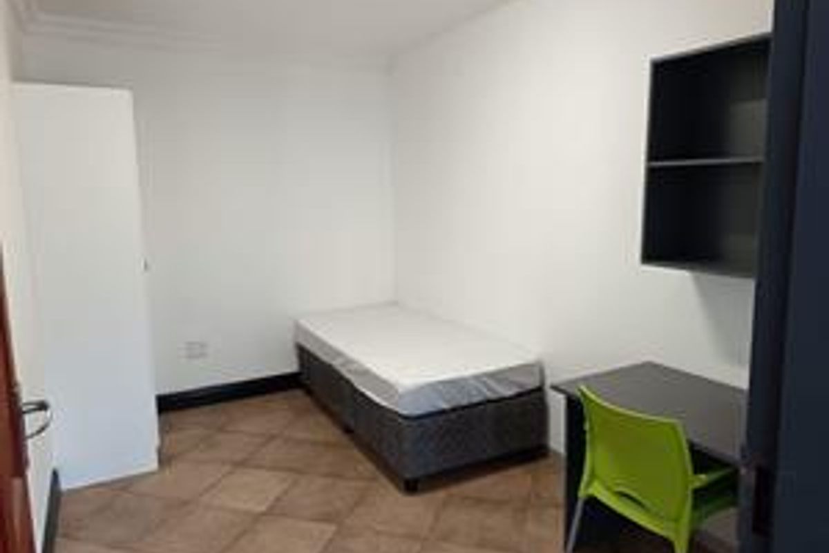 A functional bedroom featuring tiled flooring, a built-in wardrobe, and wall-mounted shelving, providing a practical living space.