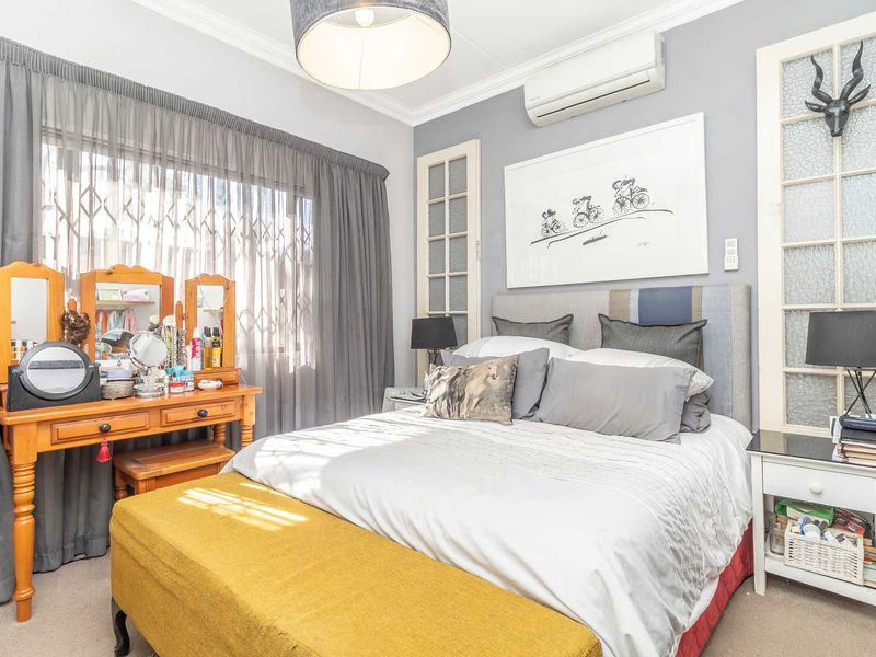 A well-maintained bedroom featuring a wall-mounted air conditioning unit, decorative glass-paneled doors, and neutral wall finishes.