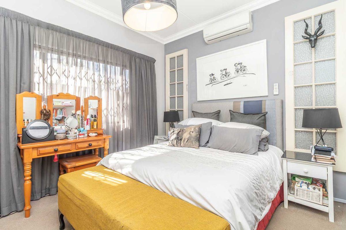 A well-maintained bedroom featuring a wall-mounted air conditioning unit, decorative glass-paneled doors, and neutral wall finishes.