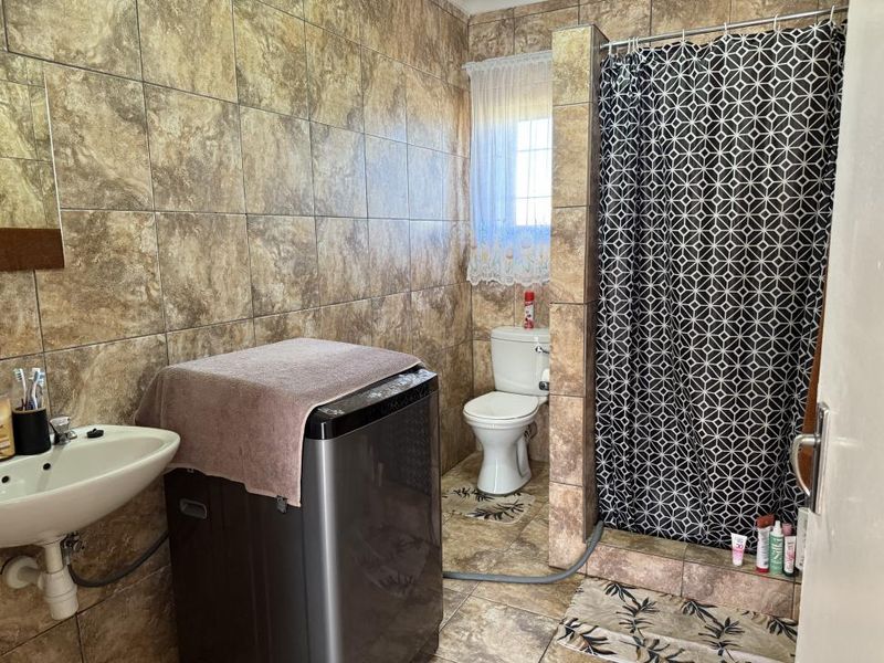 A functional bathroom featuring a tiled shower enclosure, toilet, and wall-mounted basin with full-height wall tiling.