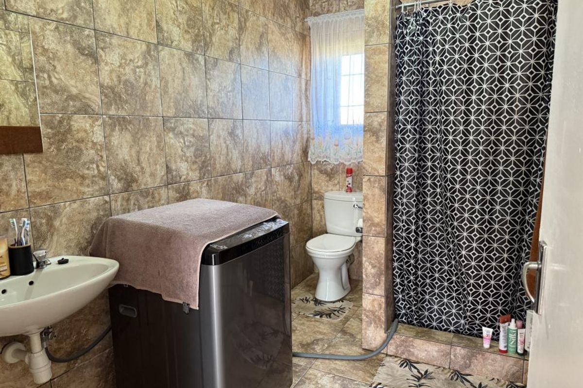 A functional bathroom featuring a tiled shower enclosure, toilet, and wall-mounted basin with full-height wall tiling.