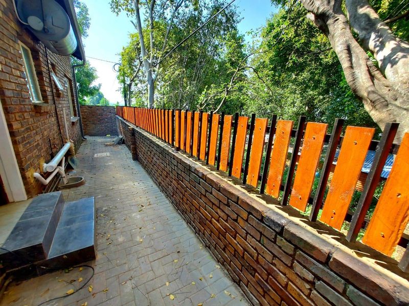 A side exterior walkway featuring a brick boundary wall with a timber slat fence, paved flooring, and external plumbing fixtures.