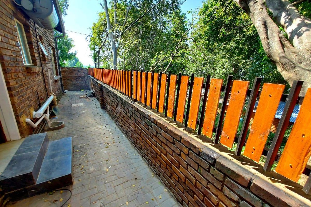 A side exterior walkway featuring a brick boundary wall with a timber slat fence, paved flooring, and external plumbing fixtures.