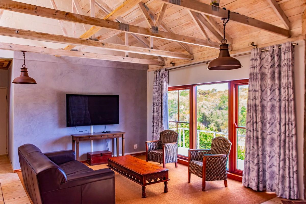 Spacious living room featuring a vaulted ceiling with exposed timber trusses, large sliding glass doors, and tiled flooring with views of the surrounding greenery.