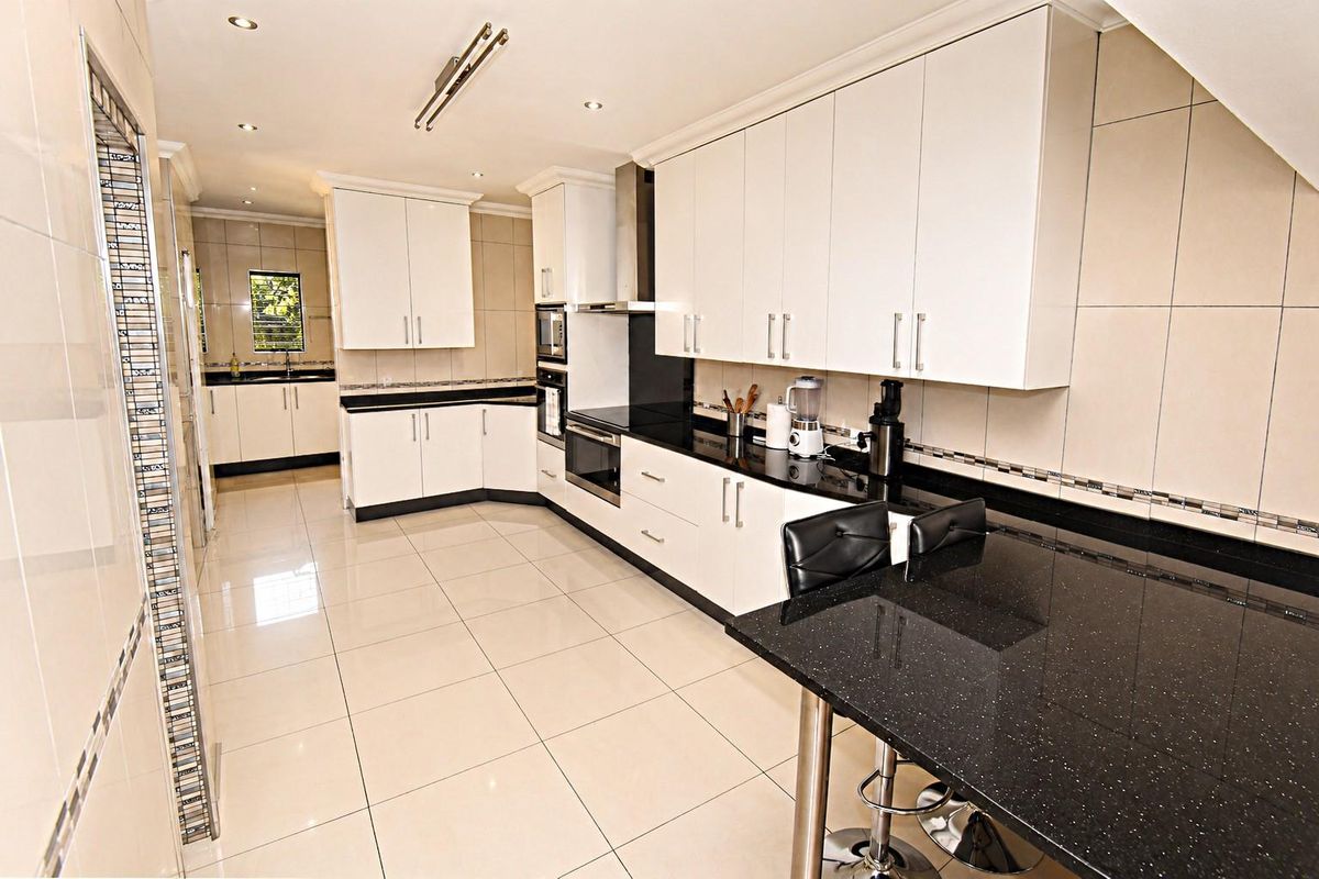 Modern kitchen featuring white cabinetry, black granite countertops, built-in appliances, and polished tiled flooring with an integrated breakfast bar.