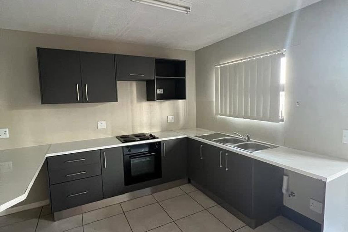 A clean, modern kitchen featuring dark grey cabinetry, white countertops, built-in oven and hob, and neutral tiled flooring.