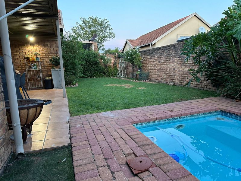 Private backyard featuring a swimming pool, paved patio area, and a well-maintained lawn enclosed by brick boundary walls.