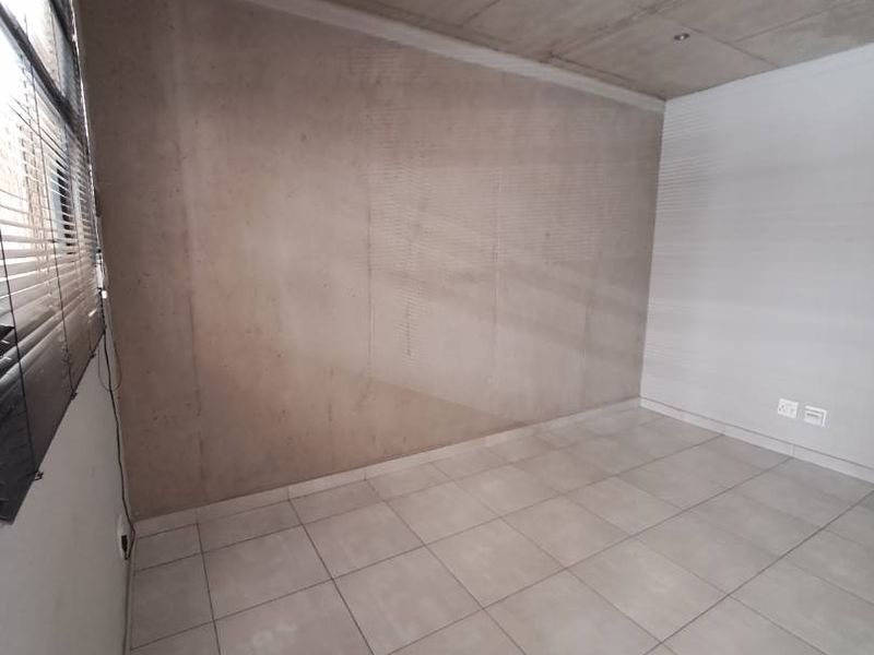 An empty bedroom featuring modern exposed concrete ceilings, neutral tiled flooring, and venetian blinds, offering a clean and contemporary blank canvas.