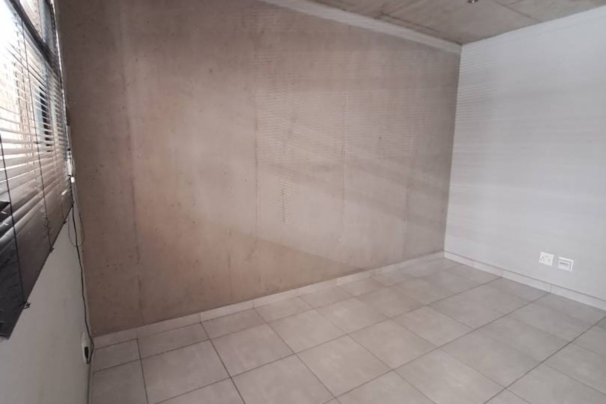 An empty bedroom featuring modern exposed concrete ceilings, neutral tiled flooring, and venetian blinds, offering a clean and contemporary blank canvas.
