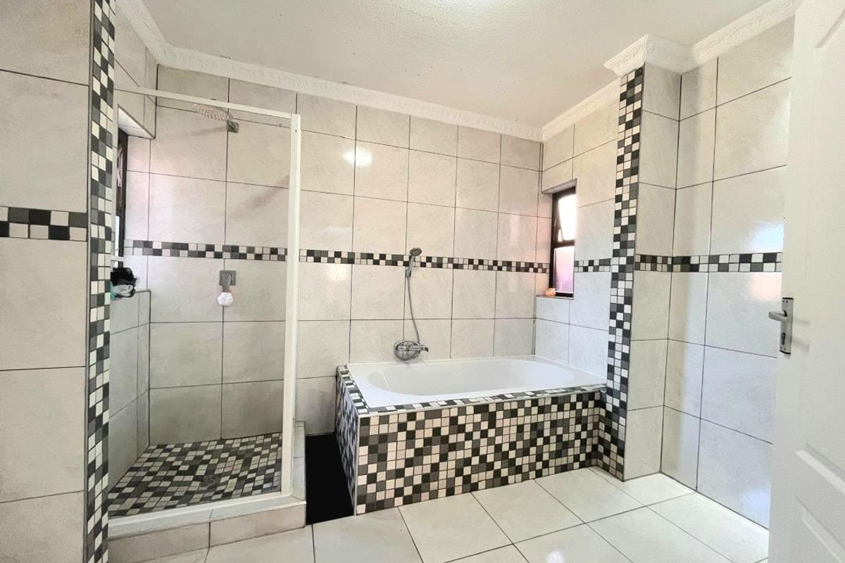 A functional bathroom featuring a built-in bathtub, a separate glass-enclosed shower, and decorative checkered tile accents throughout the space.