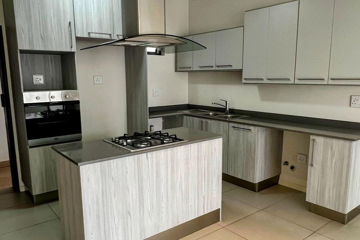 Modern kitchen featuring light wood-grain cabinetry, stone countertops, a central island with a gas hob, and integrated stainless steel appliances.