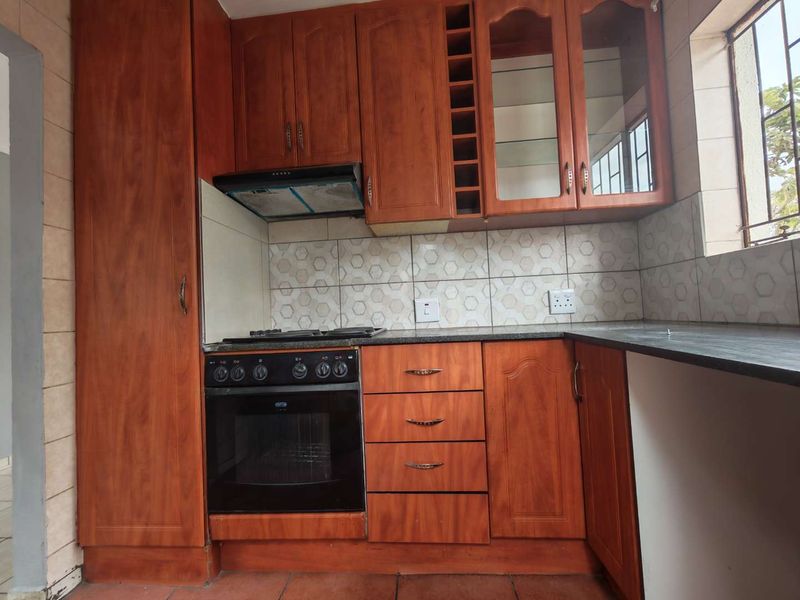 A functional kitchen featuring wooden cabinetry, built-in oven, hob, extractor fan, and tiled backsplash with a window providing natural light.