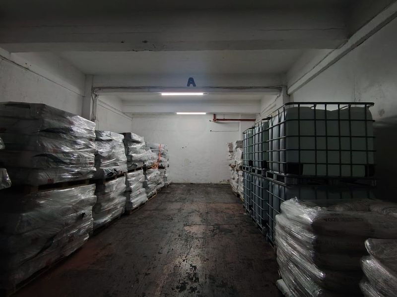 Industrial storage unit featuring concrete flooring, exposed ceiling beams, and functional overhead fluorescent lighting, suitable for warehouse or logistics operations.