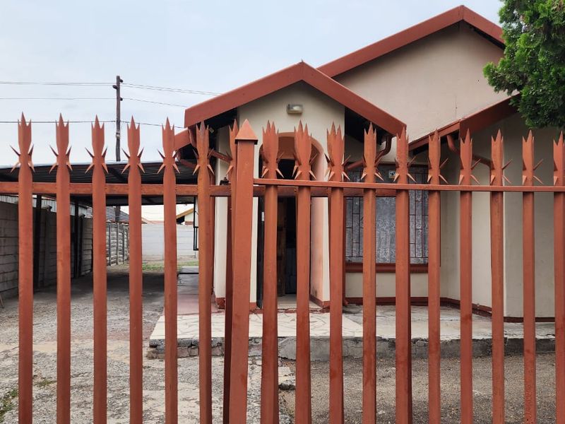 Front view of a single-story house featuring a metal security fence, a carport, and a concrete driveway.