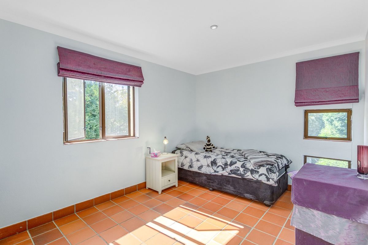 A bedroom featuring terracotta floor tiles, timber-framed windows, and recessed downlighting, offering a functional space with natural light.