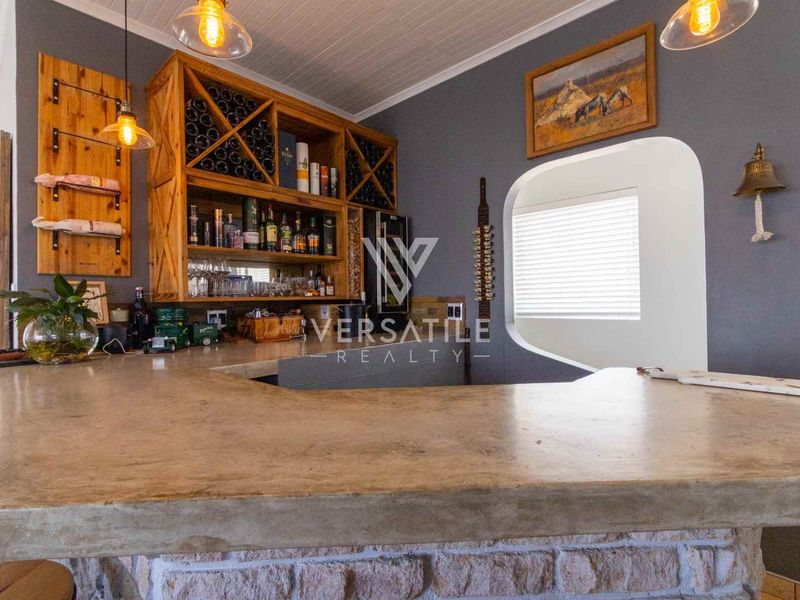 A well-appointed home bar featuring a solid concrete countertop, stone-clad base, custom timber wine storage, and decorative pendant lighting.