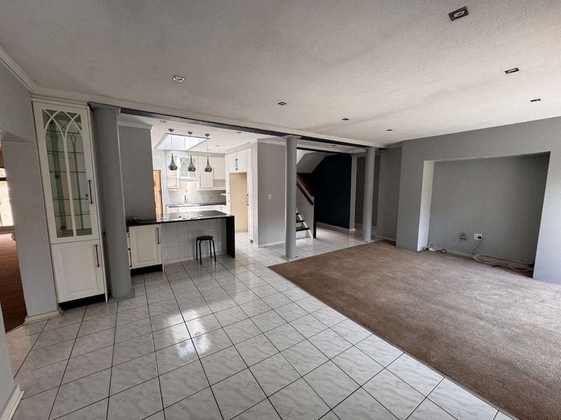 Spacious open-plan living and kitchen area featuring tiled and carpeted flooring, built-in cabinetry, and structural columns, offering a versatile layout for modern living.