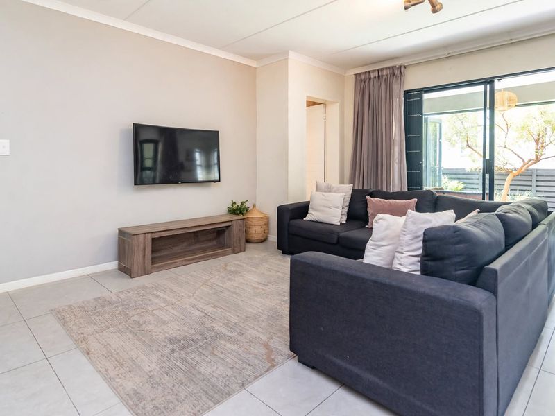 A bright living room featuring neutral tiled flooring, a wall-mounted television area, and large sliding glass doors providing access to the outdoor space.