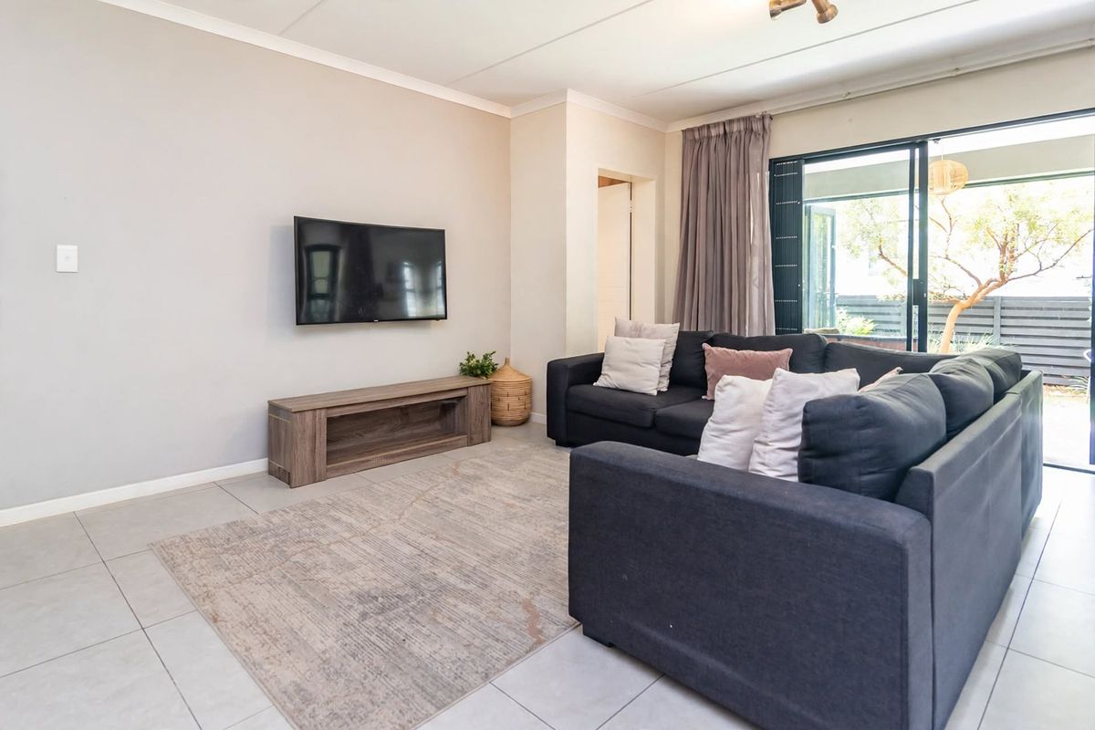 A bright living room featuring neutral tiled flooring, a wall-mounted television area, and large sliding glass doors providing access to the outdoor space.