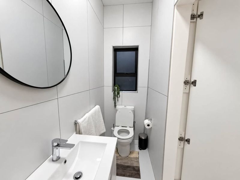 A modern, compact bathroom featuring floor-to-ceiling white tiling, a sleek wall-mounted basin with chrome fixtures, and a contemporary toilet.