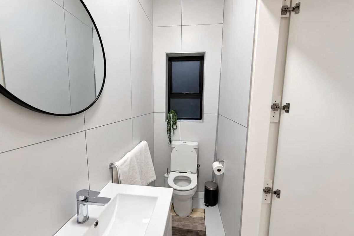 A modern, compact bathroom featuring floor-to-ceiling white tiling, a sleek wall-mounted basin with chrome fixtures, and a contemporary toilet.