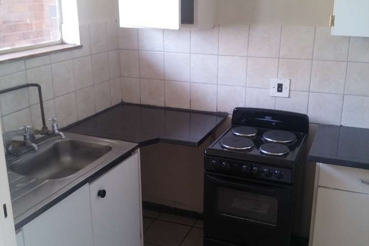 A compact, functional kitchen featuring tiled splashbacks, laminate countertops, a stainless steel sink, and a freestanding stove, offering potential for modernization.