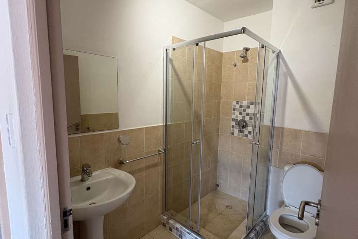 A functional bathroom featuring a glass-enclosed shower, pedestal basin, and toilet with neutral tiled flooring and wall accents.
