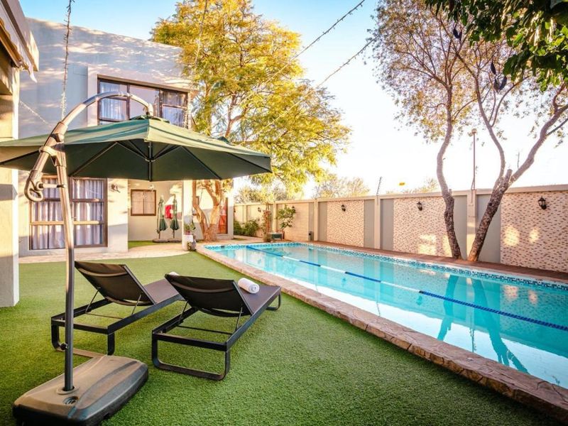 A well-maintained outdoor pool area featuring a lap pool with stone coping, surrounded by artificial turf and a secure perimeter wall.