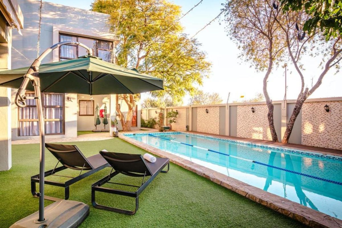 A well-maintained outdoor pool area featuring a lap pool with stone coping, surrounded by artificial turf and a secure perimeter wall.