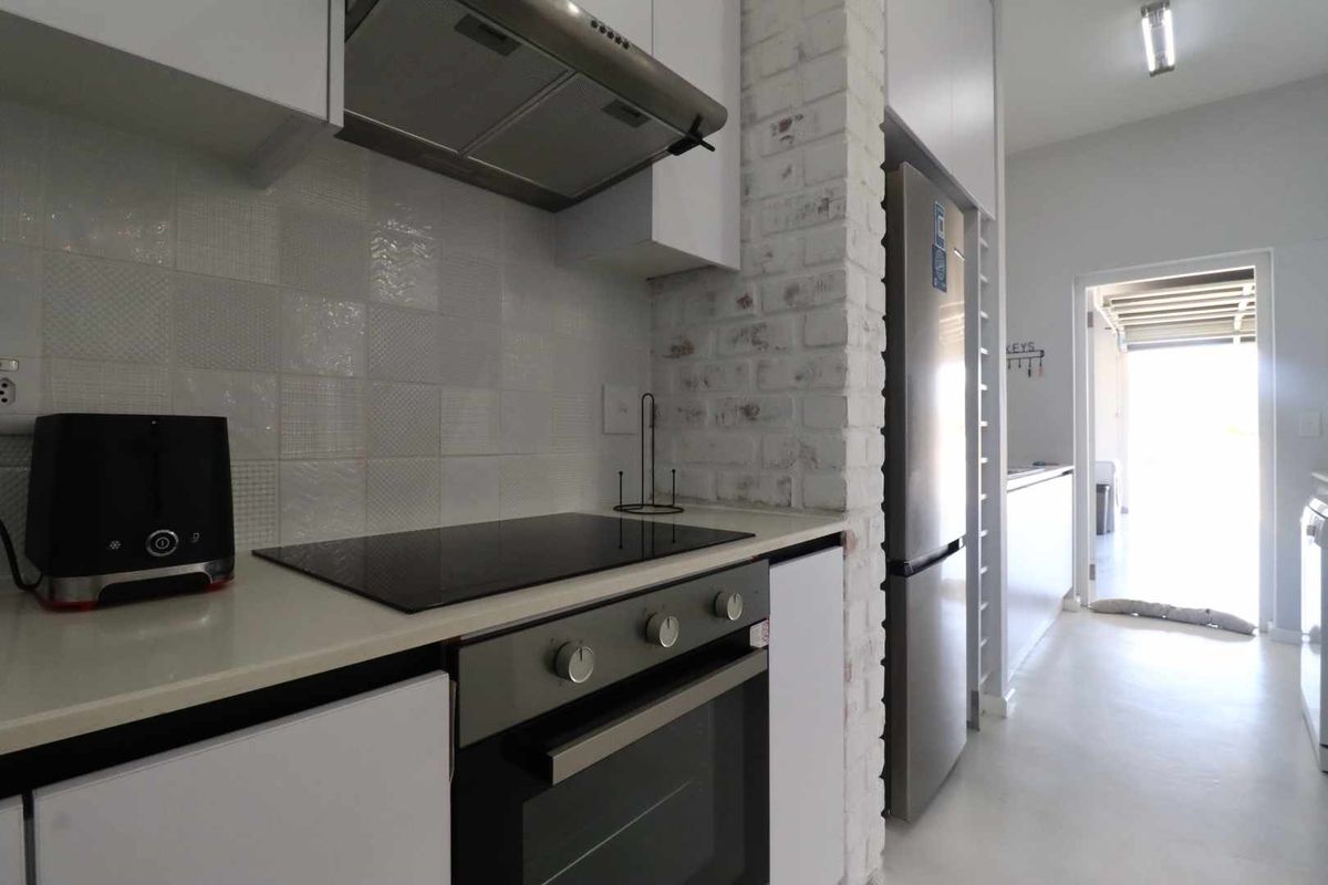 Modern kitchen featuring a built-in oven, induction hob, extractor fan, and white cabinetry, with a distinctive exposed brick pillar and tiled backsplash.