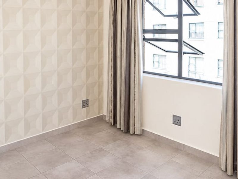 A bright, empty bedroom featuring neutral textured wallpaper, modern grey floor tiles, and a contemporary pendant light fixture.