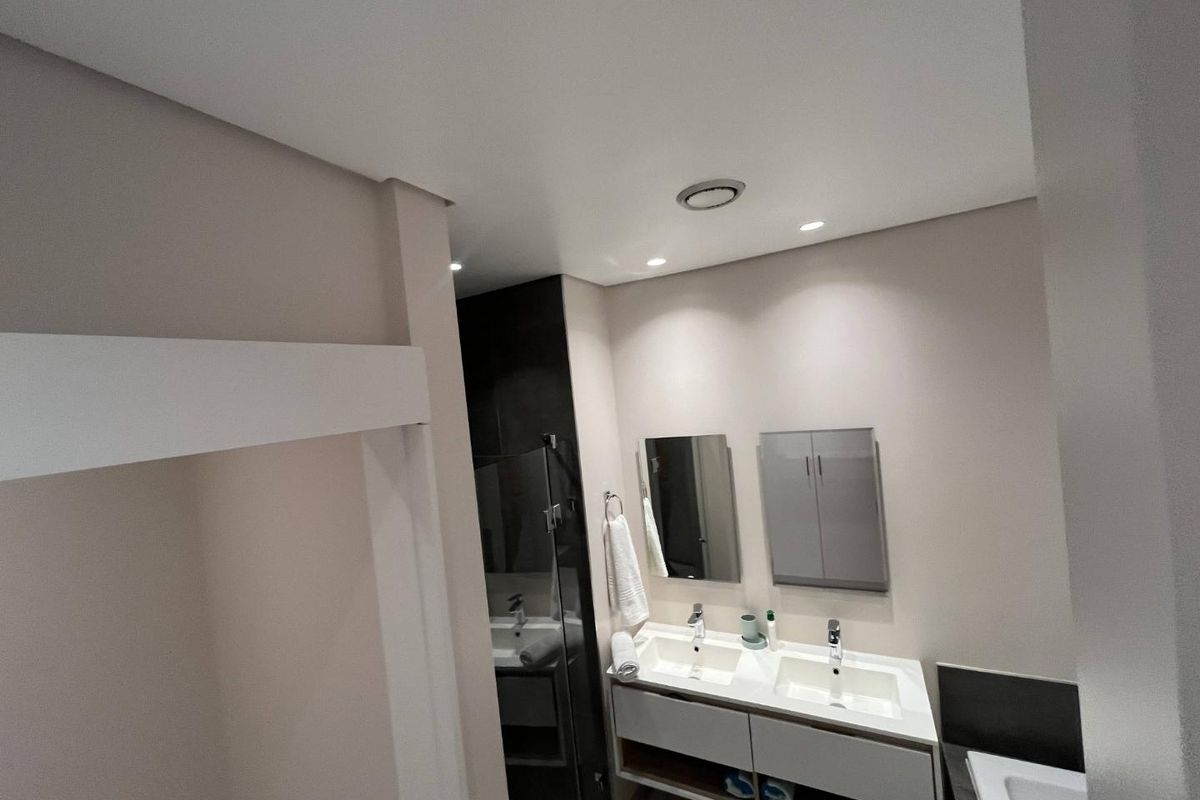 Modern bathroom featuring a double vanity with integrated sinks, wall-mounted mirrors, and a glass-enclosed shower area with contemporary finishes.