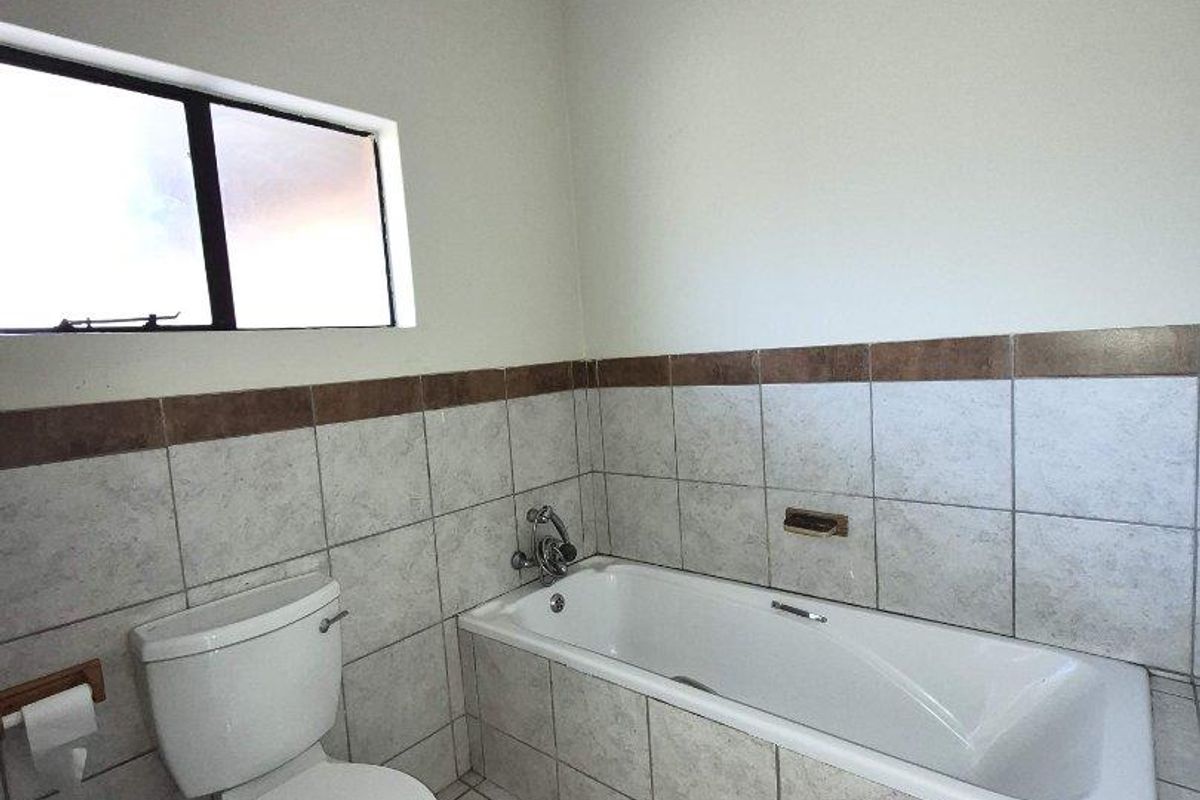 A functional bathroom featuring a standard bathtub, toilet, and neutral wall and floor tiling with a decorative border.
